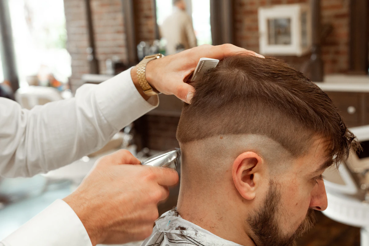 Barbier en chemise blanche coupant les cheveux d'un client au ciseau